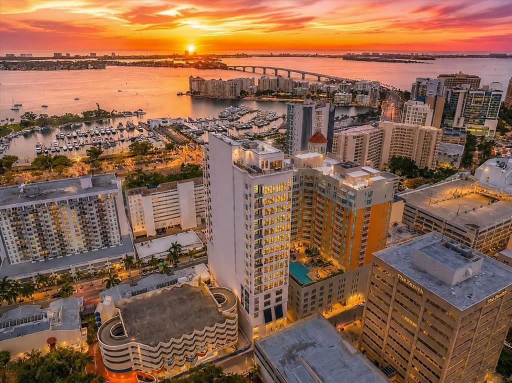 An aerial view of a tall residential tower at sunset near a waterfront city — 33 S PALM AVENUE UNIT 901, SARASOTA, FL