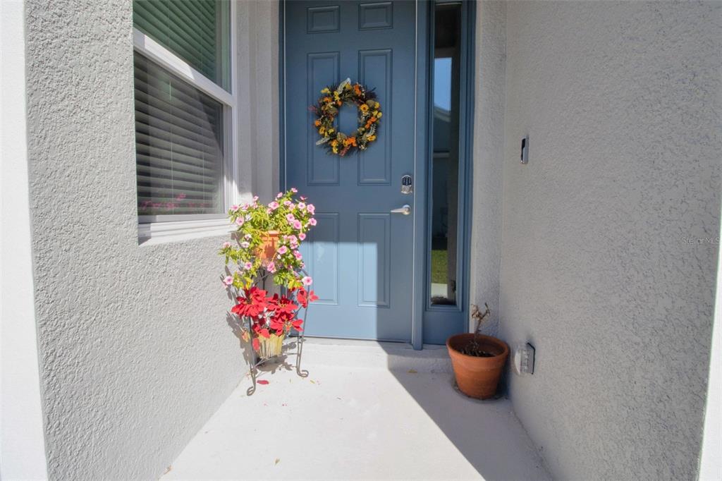 A blue front door with a wreath stands on a concrete porch with potted plants — 1755 NOTTINGHAM TRAIL, PORT CHARLOTTE, FL