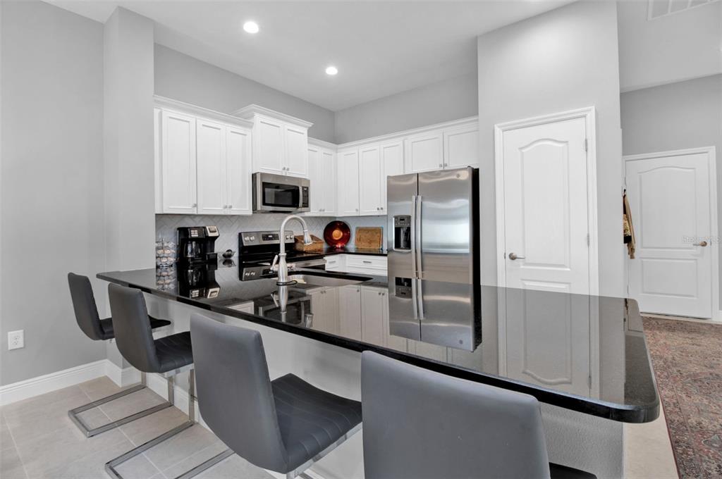 A kitchen features white cabinets, stainless steel appliances, and a black countertop island with stools — 1755 NOTTINGHAM TRAIL, PORT CHARLOTTE, FL