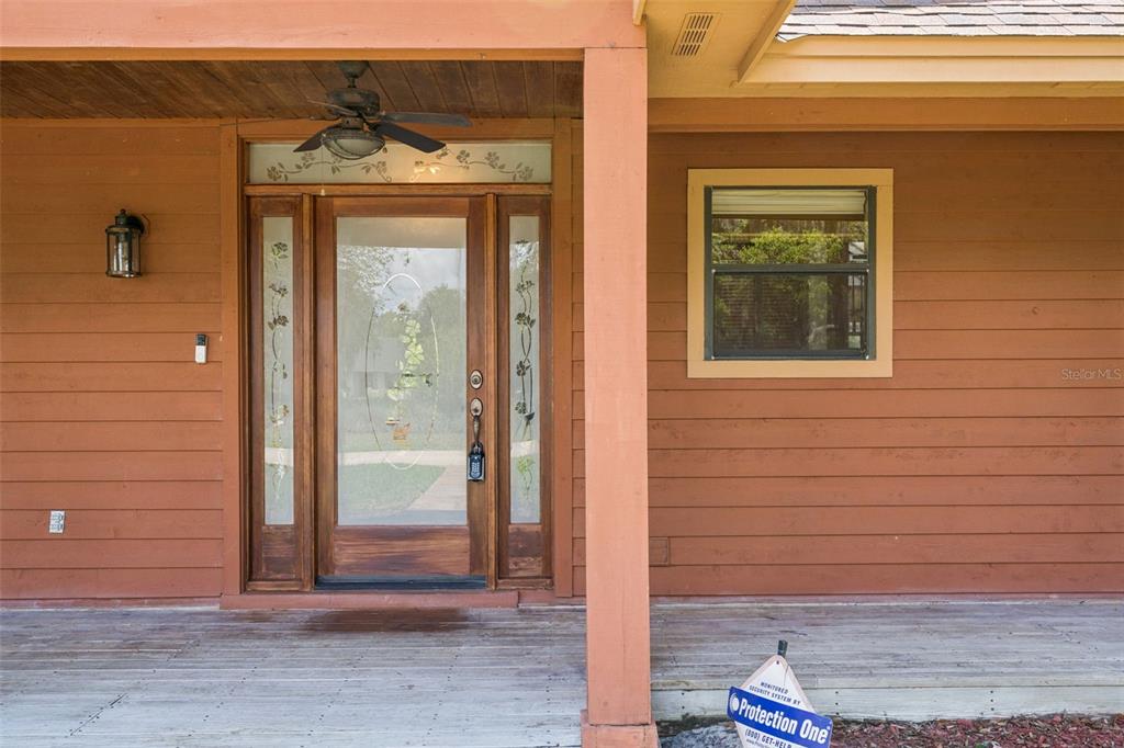 A wooden front porch features a glass-paneled door, a ceiling fan, and a security sign — 15010 MILL POND ROAD, TAVARES, FL
