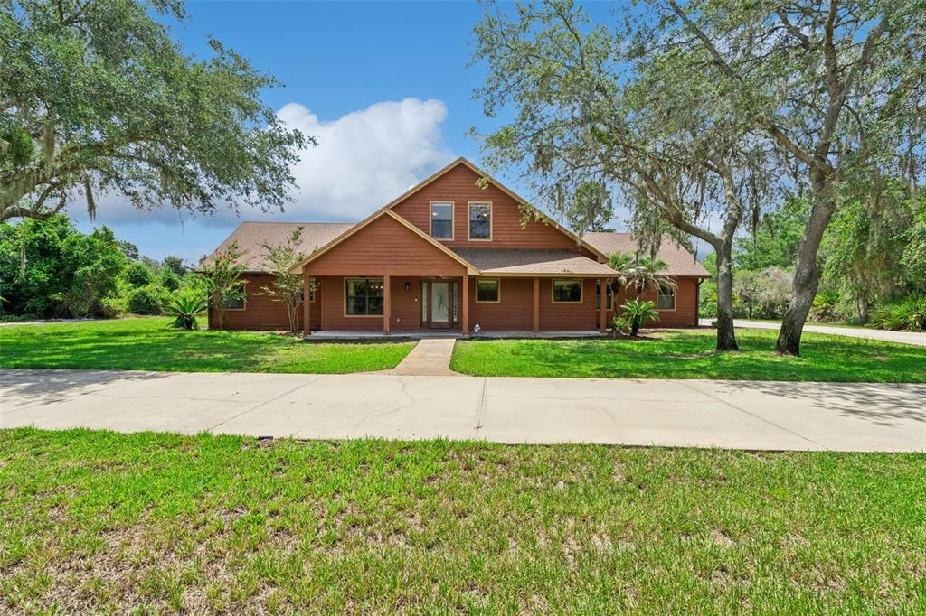 A brown, two-story house with a covered porch sits behind a large concrete driveway — 15010 MILL POND ROAD, TAVARES, FL