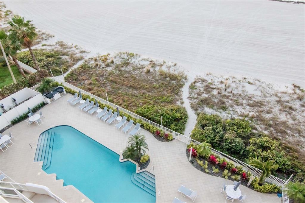 An aerial view shows a swimming pool on a patio next to a sandy beach — 1350 GULF BOULEVARD UNIT 703, CLEARWATER BEACH, FL