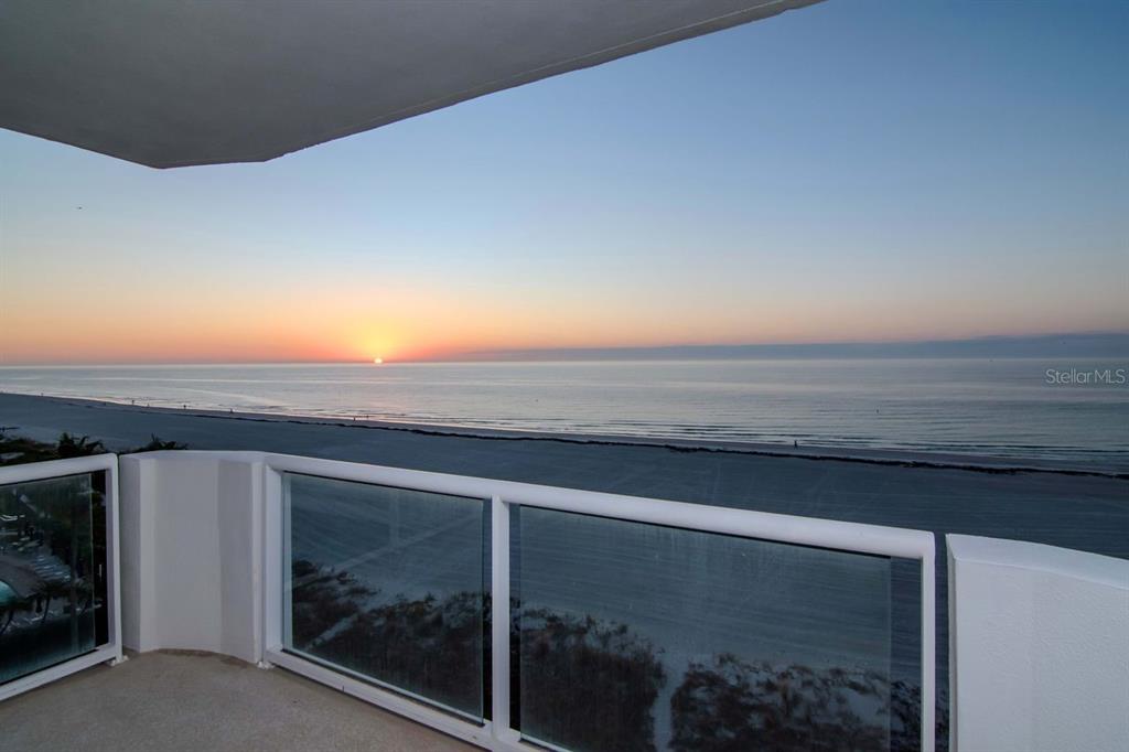 A balcony with a glass railing overlooks a beach at sunset — 1350 GULF BOULEVARD UNIT 703, CLEARWATER BEACH, FL