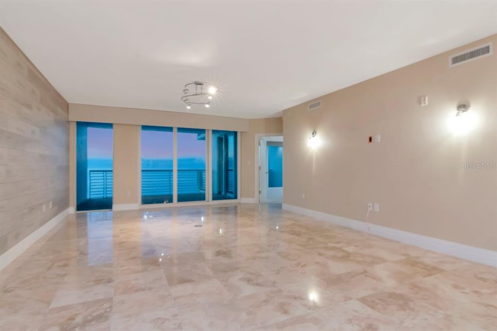 A spacious living room features light marble flooring, a wood-paneled wall, and floor-to-ceiling windows — 1350 GULF BOULEVARD UNIT 703, CLEARWATER BEACH, FL