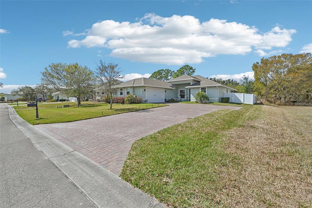 A single-story house with a brick driveway and a white fence under a blue sky — 3955 OAK HOLLOW AVENUE, VERO BEACH, FL