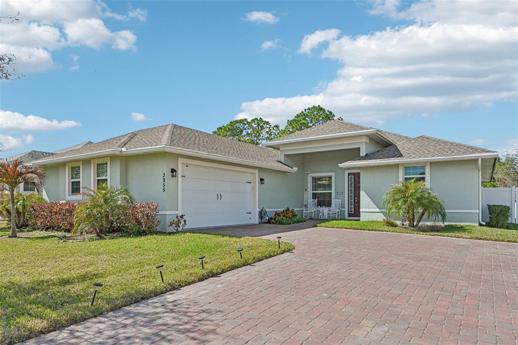 A single-story house with a light green exterior, a brick driveway, and a two-car garage — 3955 OAK HOLLOW AVENUE, VERO BEACH, FL