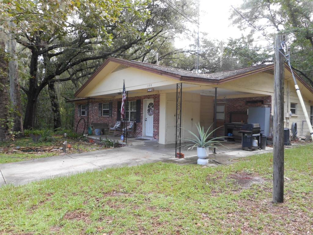 A single-story brick house with a covered front porch and a carport under a large tree — 1135 SW SHOREWOOD DRIVE, DUNNELLON, FL