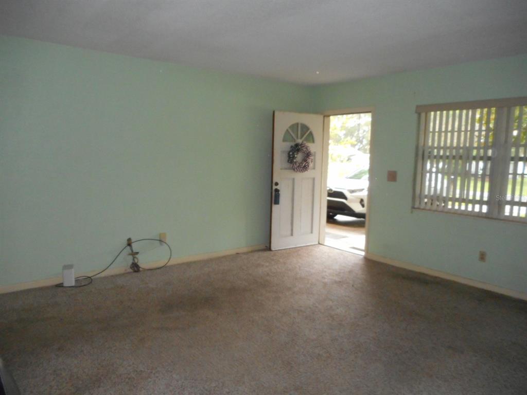 An empty room with light green walls, beige carpet, a front door, and a window — 1135 SW SHOREWOOD DRIVE, DUNNELLON, FL