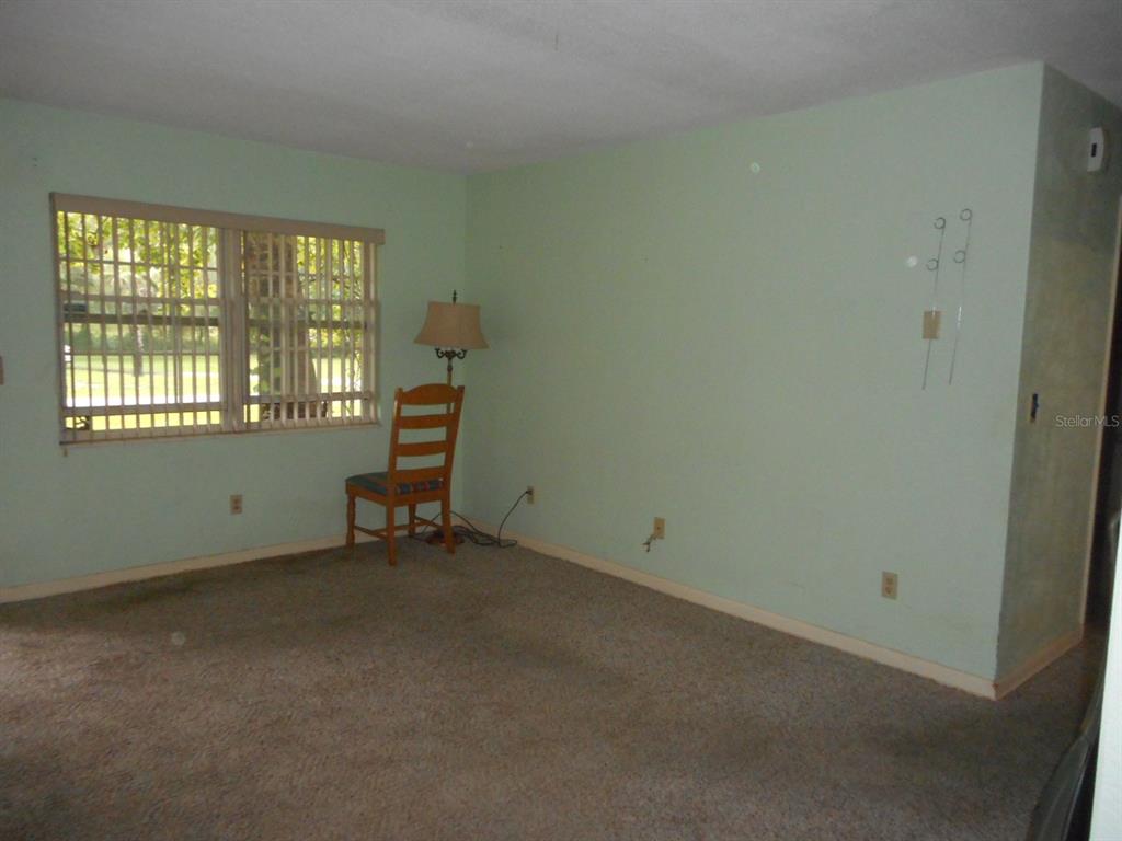 An empty room with light green walls, beige carpeting, a window with blinds, and a chair — 1135 SW SHOREWOOD DRIVE, DUNNELLON, FL