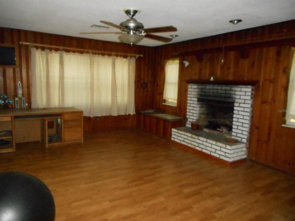 A living room with wood-paneled walls, a brick fireplace, and a light-colored wood floor — 1135 SW SHOREWOOD DRIVE, DUNNELLON, FL