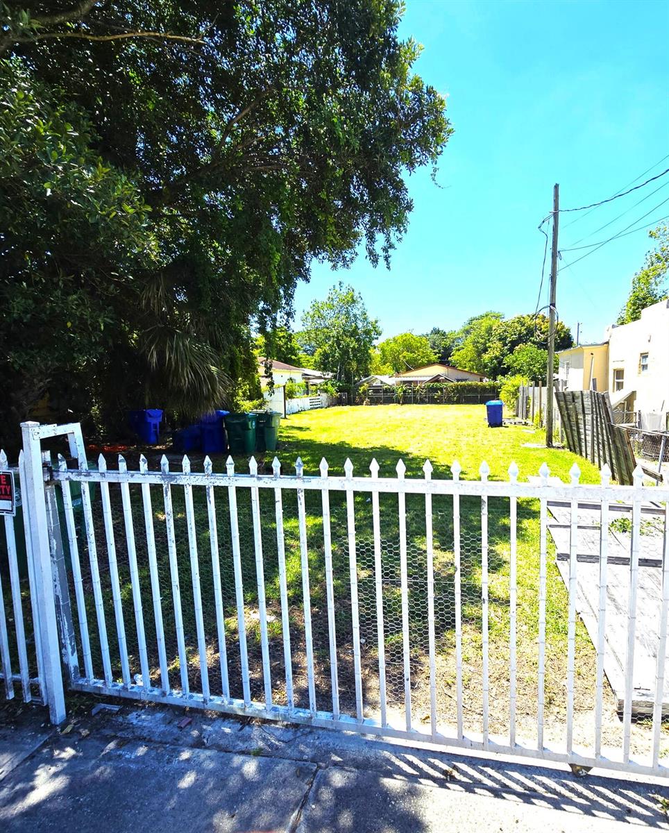A white metal gate opens to a vacant, grassy residential lot with scattered trash bins — 1252 NW 35th Street, Miami FL 33142, MIAMI, FL