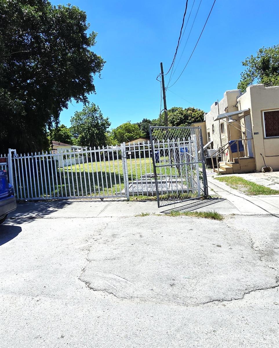 A white metal fence encloses a vacant lot next to a small residential building — 1252 NW 35th Street, Miami FL 33142, MIAMI, FL