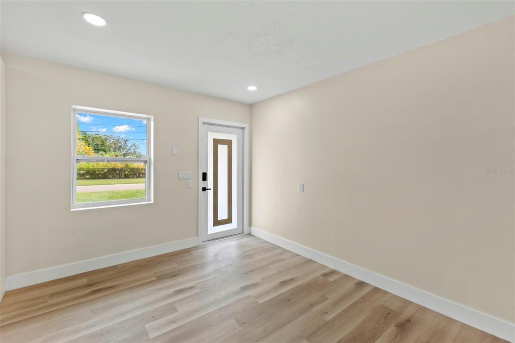 An empty room features light wood-look flooring, beige walls, a window, and a modern door — 4430 CARSON STREET NE, ST PETERSBURG, FL