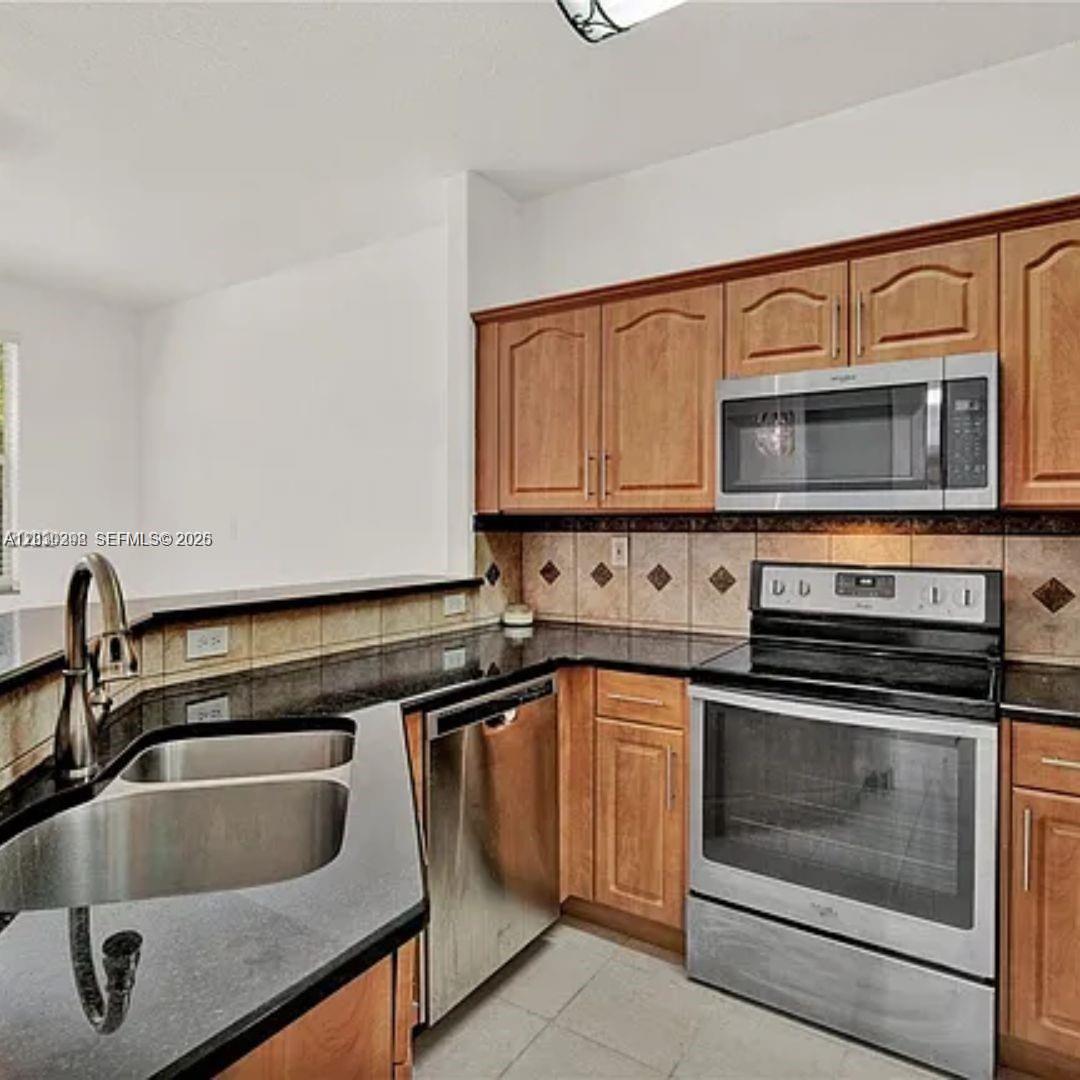 A kitchen features wood cabinets, black granite countertops, stainless steel appliances, and a tiled backsplash — 10902 NW 79th St # 10902, Doral FL 33178, DORAL, FL