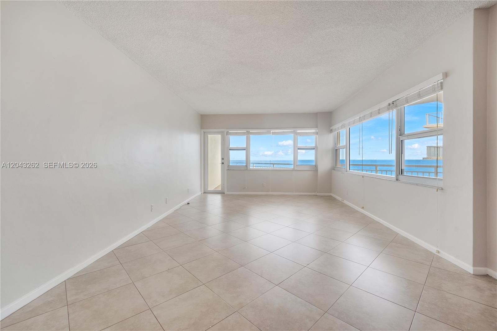 An empty room with light tile flooring and large windows overlooking the ocean — 710 N Ocean Blvd # 710, Pompano Beach FL 33062, POMPANO BEACH, FL