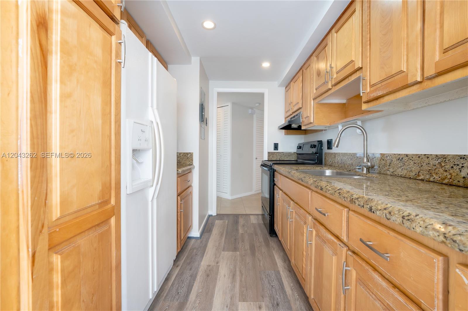A galley kitchen features wood cabinets, granite countertops, a white refrigerator, and wood-look flooring — 710 N Ocean Blvd # 710, Pompano Beach FL 33062, POMPANO BEACH, FL