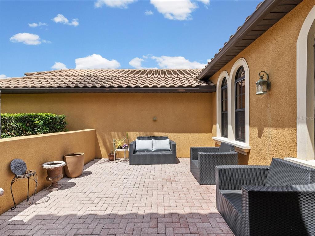 A paved patio features dark wicker outdoor furniture against a tan stucco house wall — 3708 MARBURY COURT, LAND O LAKES, FL