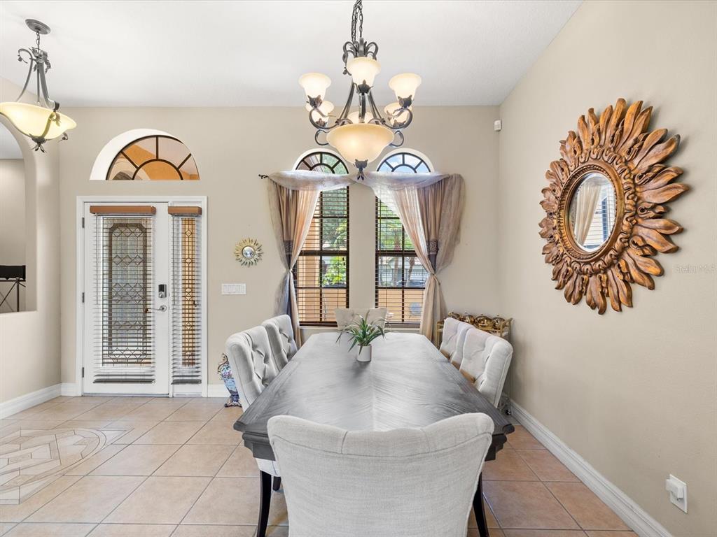A dining room features a long wooden table, upholstered chairs, a chandelier, and a sunburst mirror — 3708 MARBURY COURT, LAND O LAKES, FL