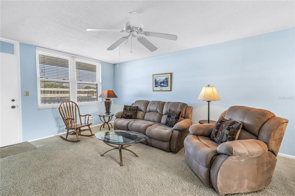 A living room features light blue walls, beige carpet, a ceiling fan, and brown furniture — 4715 BAY STREET NE UNIT 320, ST PETERSBURG, FL