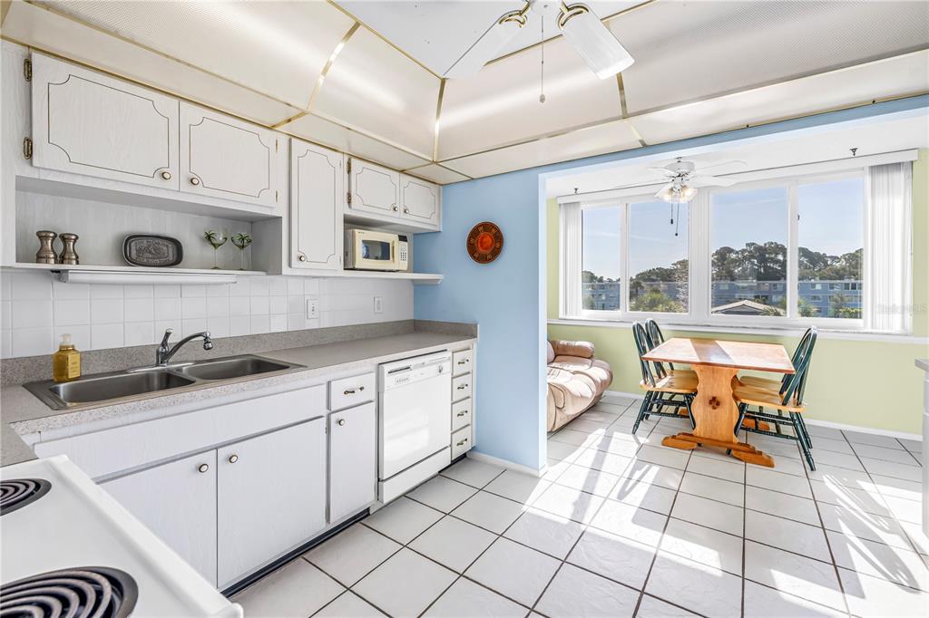 A kitchen with white cabinets and appliances features a dining area with large windows — 4715 BAY STREET NE UNIT 320, ST PETERSBURG, FL