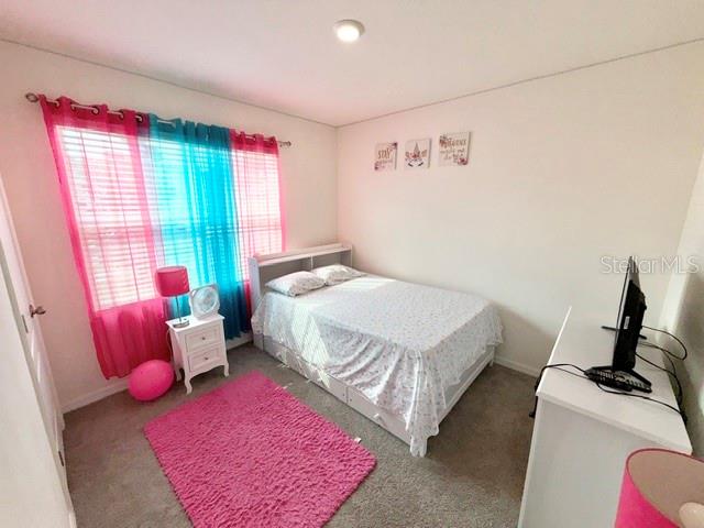 A bedroom features a bed with a patterned quilt, a pink rug, and colorful curtains — 3728 ALDER BARK LANE, SANFORD, FL