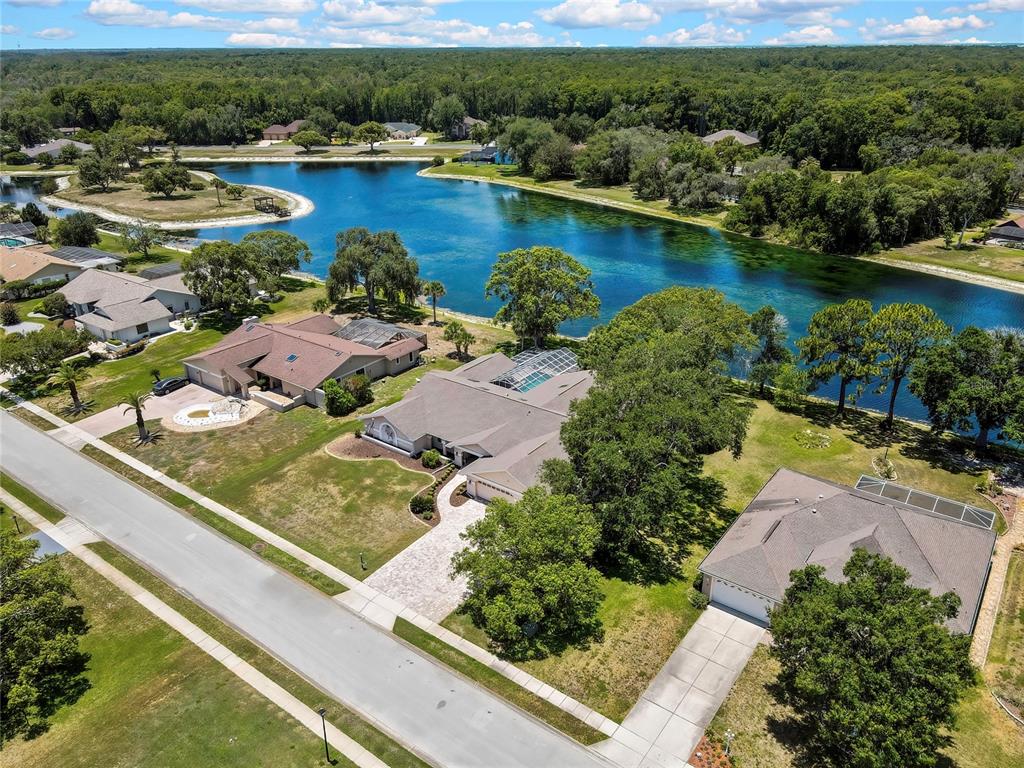 An aerial view shows three suburban houses with pools situated along a large, blue lake — 4293 RIVER BIRCH DRIVE, SPRING HILL, FL
