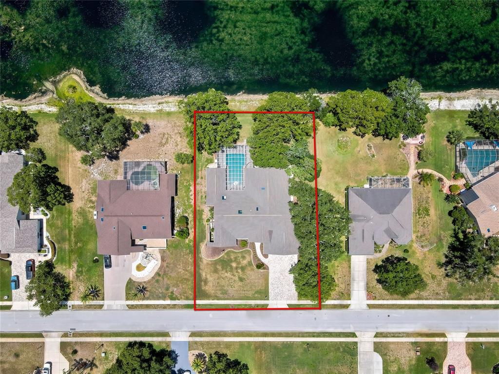 An aerial view shows a house with a screened pool on a lakefront lot — 4293 RIVER BIRCH DRIVE, SPRING HILL, FL