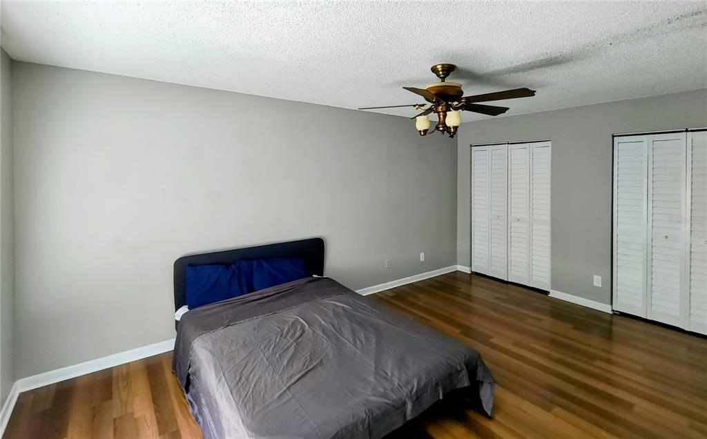 A bedroom with wood-look flooring, gray walls, a ceiling fan, and two sets of closet doors — 201 S ARRAWANA AVENUE UNIT L, TAMPA, FL