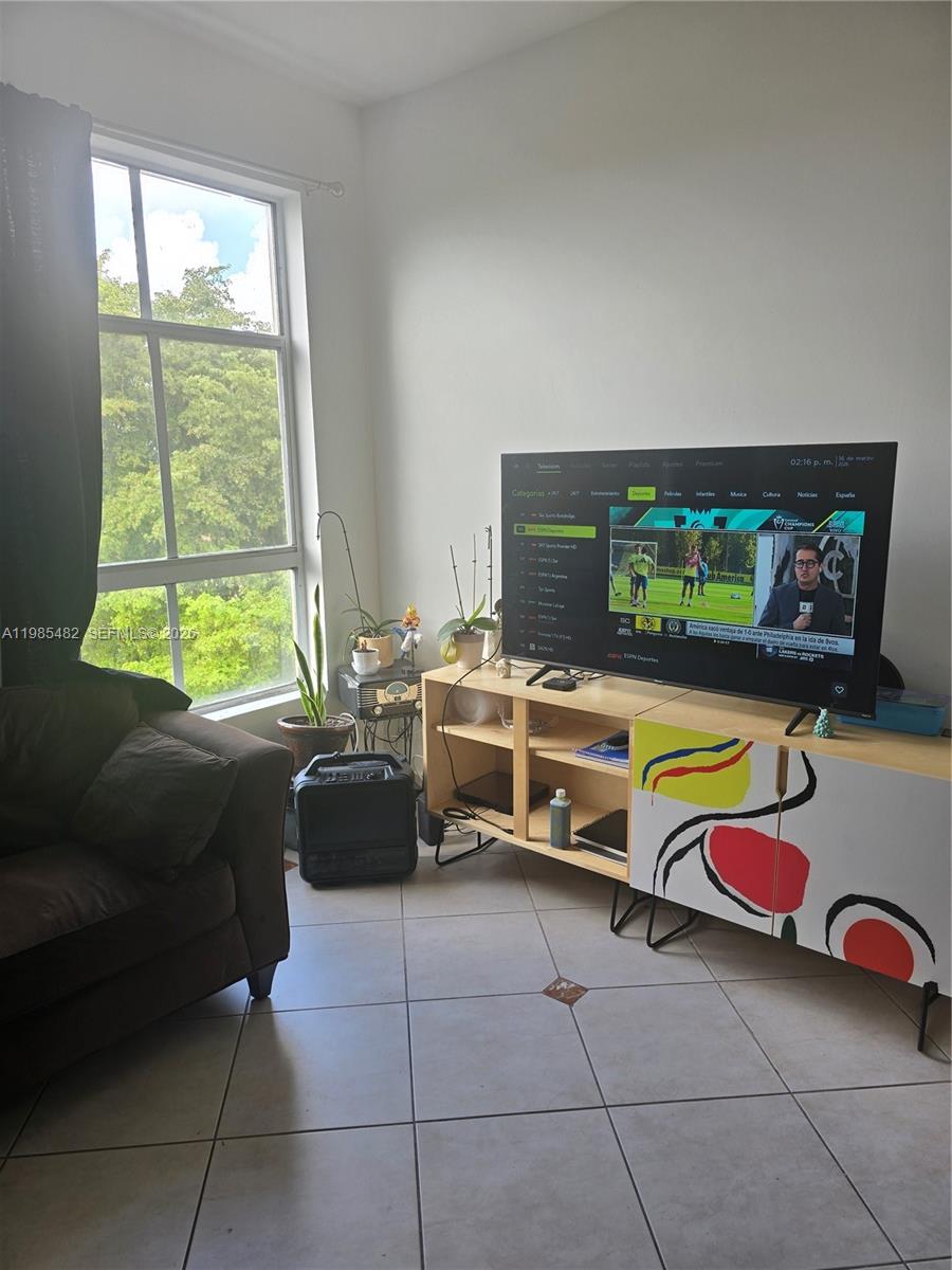 A living room features a television on a patterned cabinet, a sofa, and a large window — 7420 W 20th Ave # 451, Hialeah FL 33016, HIALEAH, FL