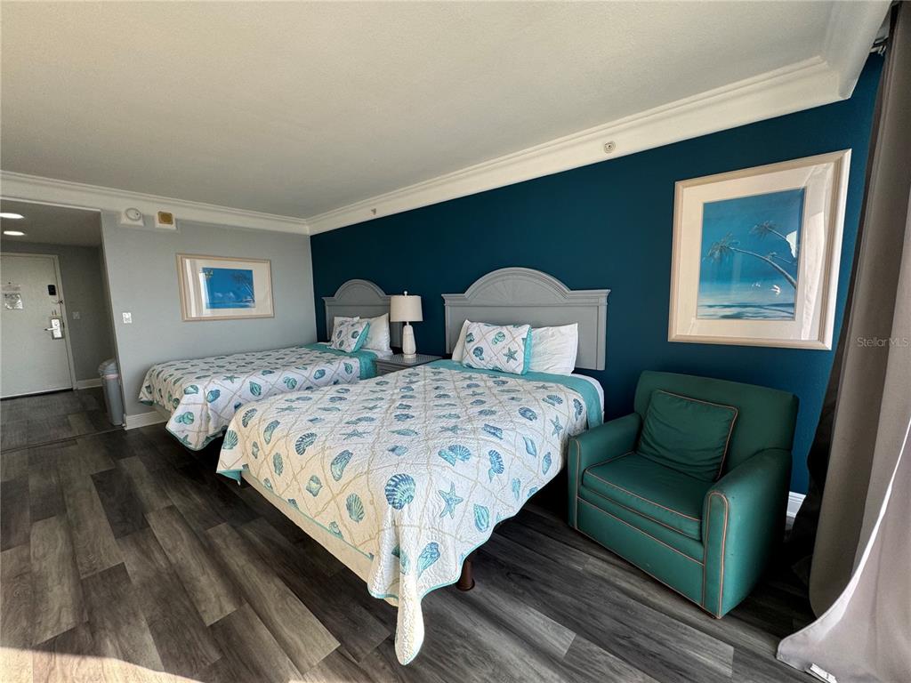 A bedroom features two beds with seashell-patterned quilts, a teal accent wall, and a green armchair — 2700 N ATLANTIC AVENUE UNIT 1003, DAYTONA BEACH, FL