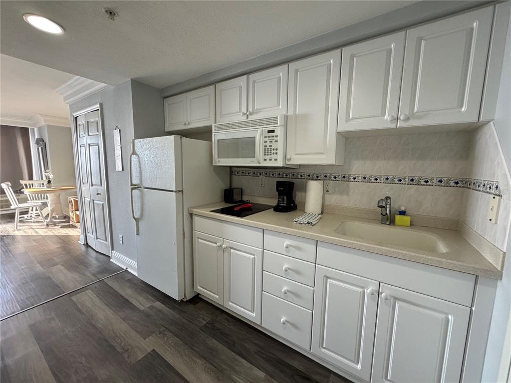 A kitchen features white cabinets, a white refrigerator, a microwave, and a beige countertop — 2700 N ATLANTIC AVENUE UNIT 1003, DAYTONA BEACH, FL