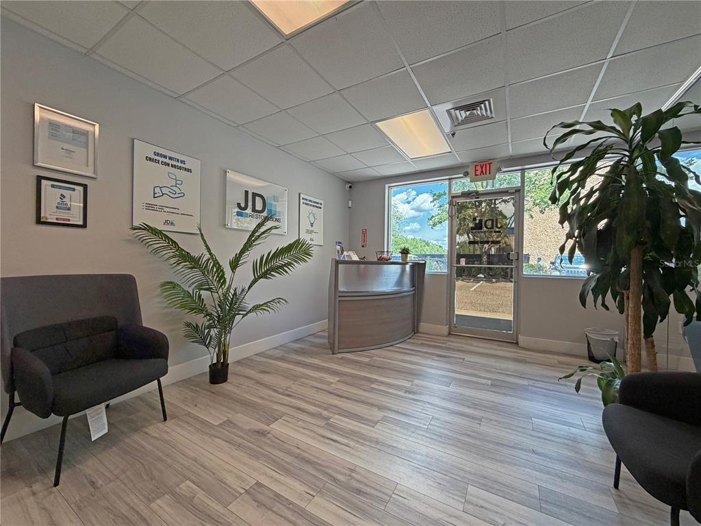 A bright office lobby features wood-look flooring, a reception desk, and two dark armchairs — 10501 S ORANGE AVENUE UNIT 107, ORLANDO, FL