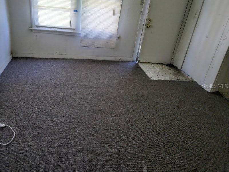 An empty room features gray carpeting, a window with white blinds, and a white door — 1102 W 13TH STREET, LAKELAND, FL