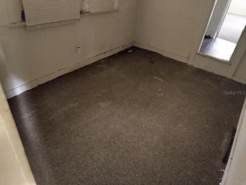 An empty room features gray carpeting, white walls, and a doorway leading to another area — 1102 W 13TH STREET, LAKELAND, FL