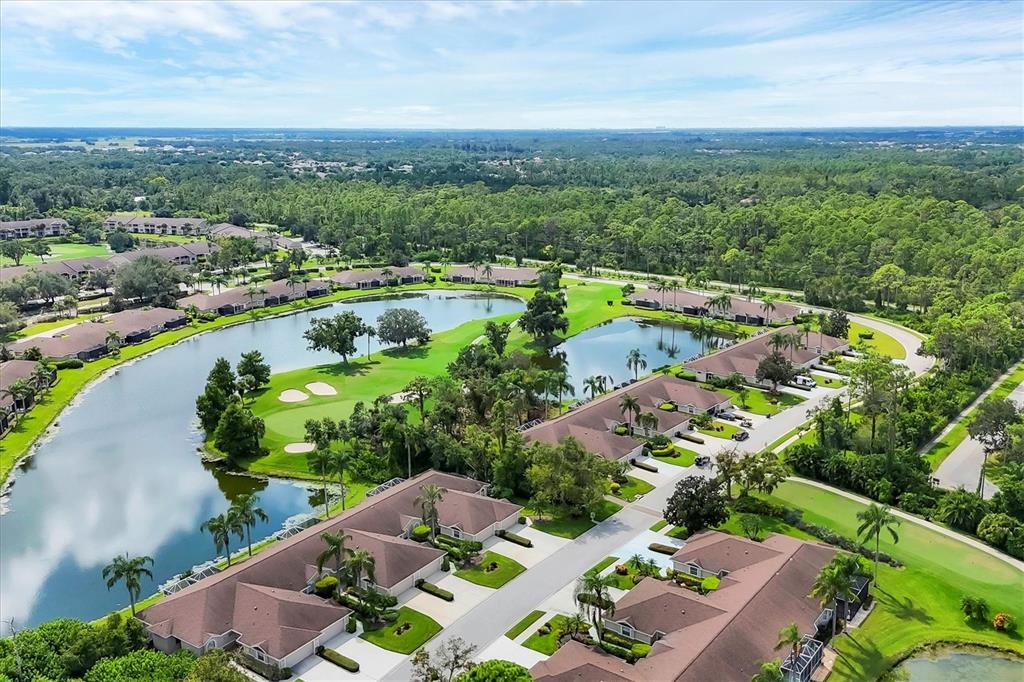 An aerial view shows residential buildings surrounding a golf course pond and lush green landscaping — 5111 PEPPERMILL COURT, SARASOTA, FL