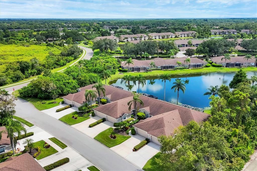 An aerial view shows a residential neighborhood with attached homes, a pond, and lush landscaping — 5111 PEPPERMILL COURT, SARASOTA, FL