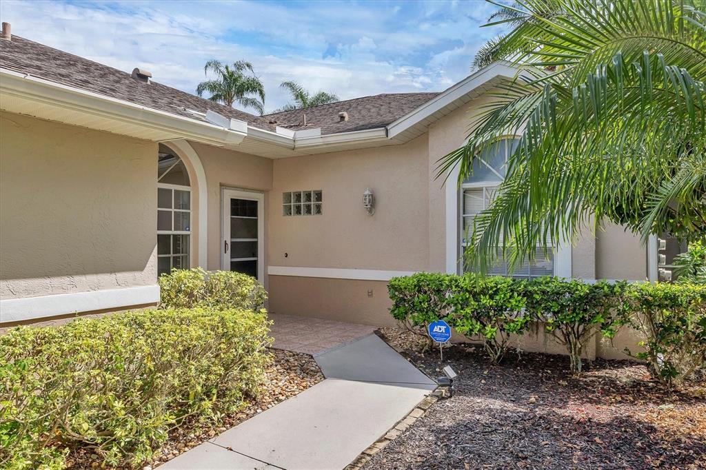 A concrete walkway leads to the front entrance of a beige house with arched windows — 5111 PEPPERMILL COURT, SARASOTA, FL