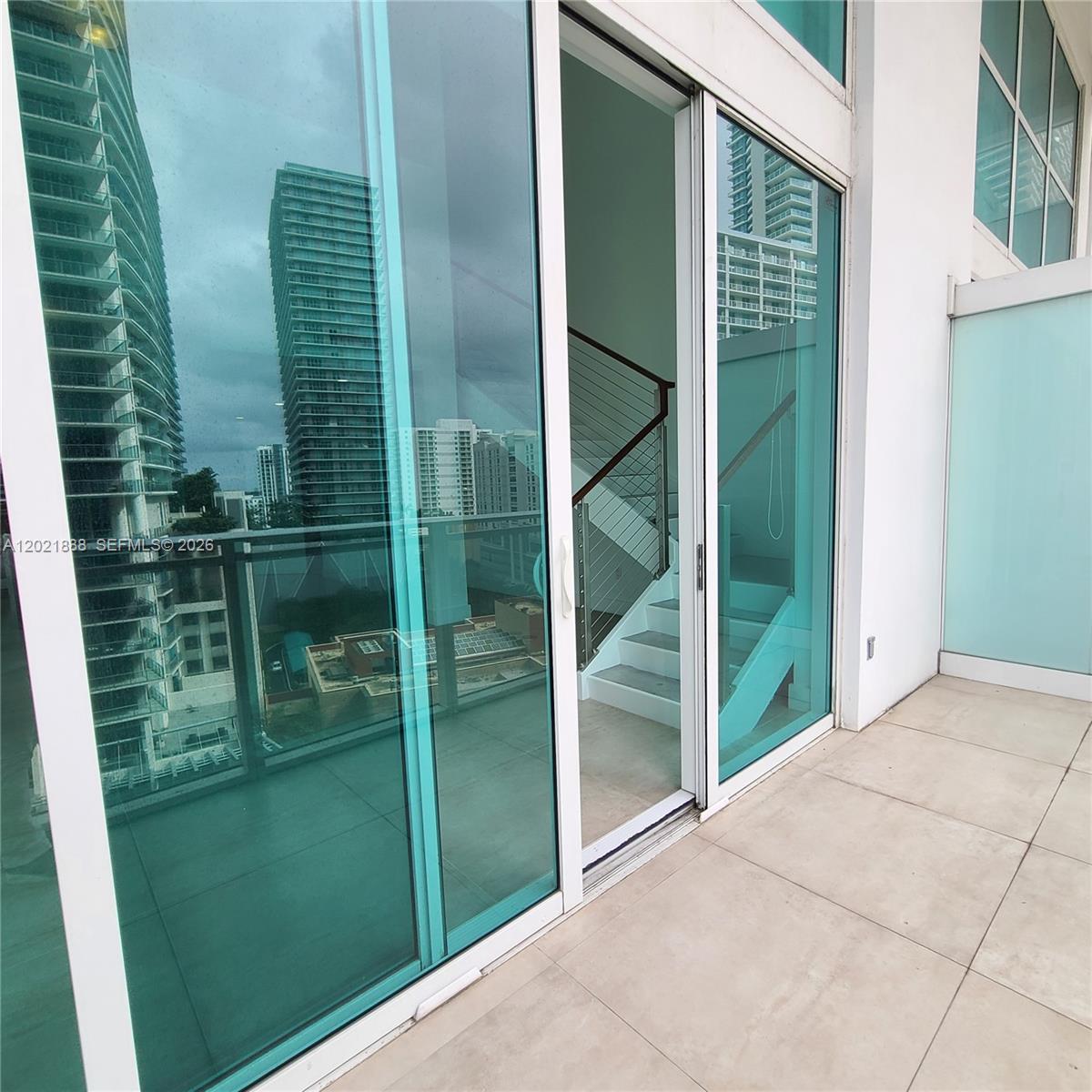A balcony with tiled flooring overlooks city buildings through large sliding glass doors — 1080 Brickell Ave # 1101, Miami FL 33131, MIAMI, FL