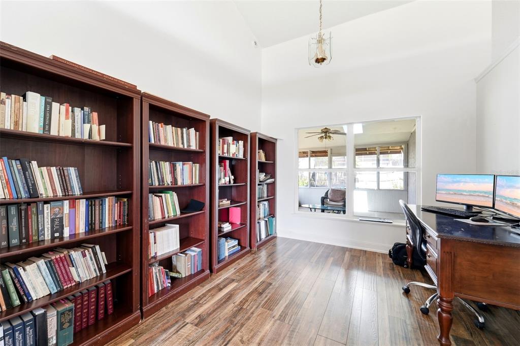 A home office features wood-look flooring, multiple dark wood bookshelves, and a dual-monitor desk setup — 1176 LYRIC DRIVE, DELTONA, FL