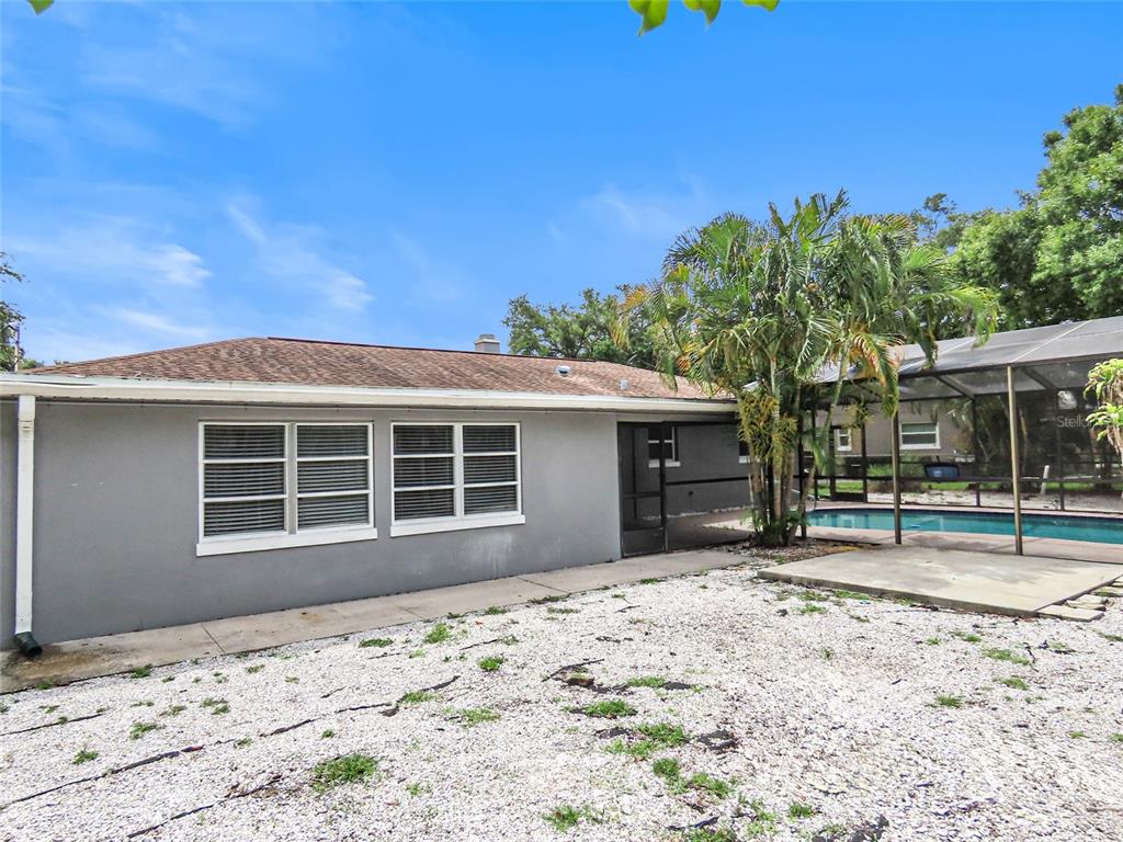 A gray house exterior with a gravel yard, a swimming pool, and a screened enclosure — 2434 65TH STREET N, ST PETERSBURG, FL