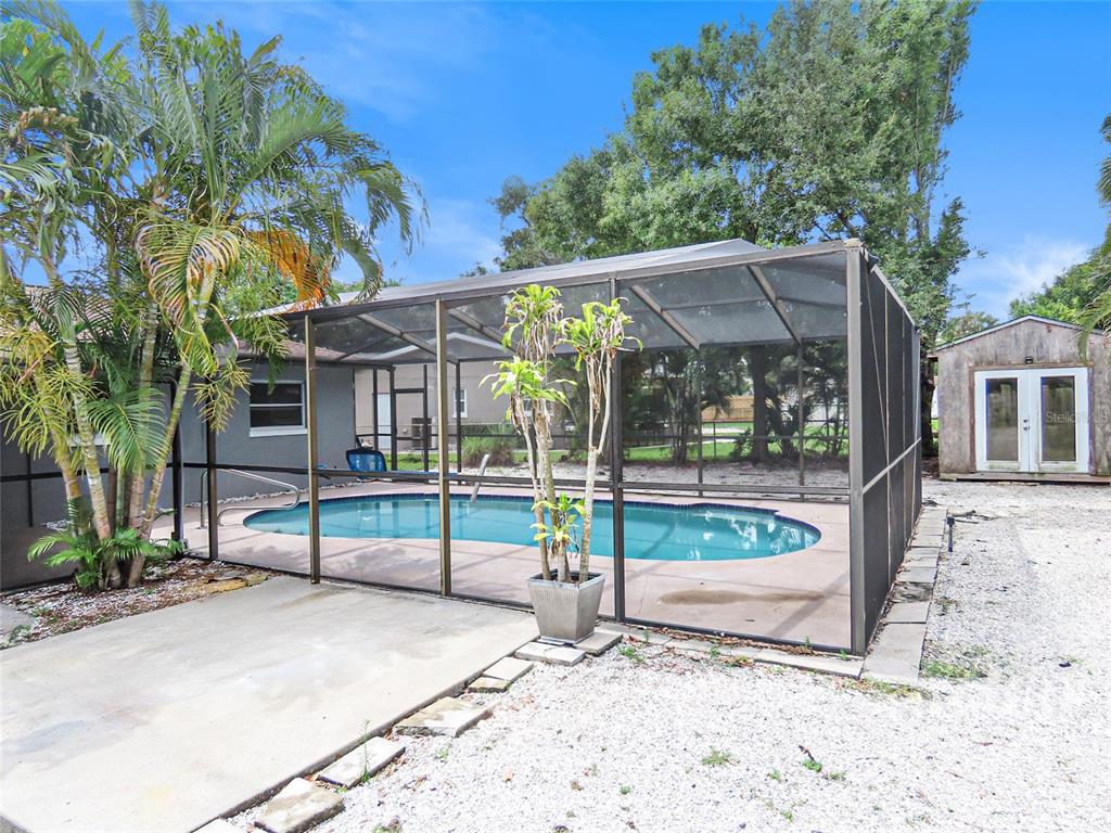 An outdoor swimming pool is enclosed by a screened lanai next to a storage shed — 2434 65TH STREET N, ST PETERSBURG, FL