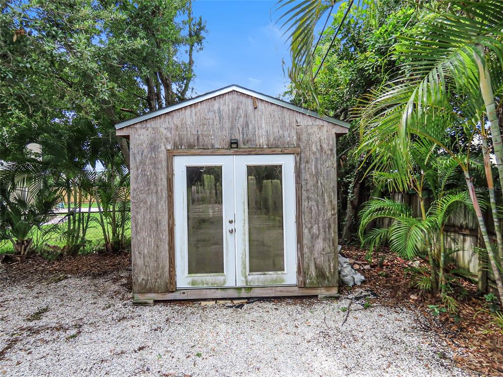A weathered wooden shed with double glass doors stands on a gravel yard — 2434 65TH STREET N, ST PETERSBURG, FL