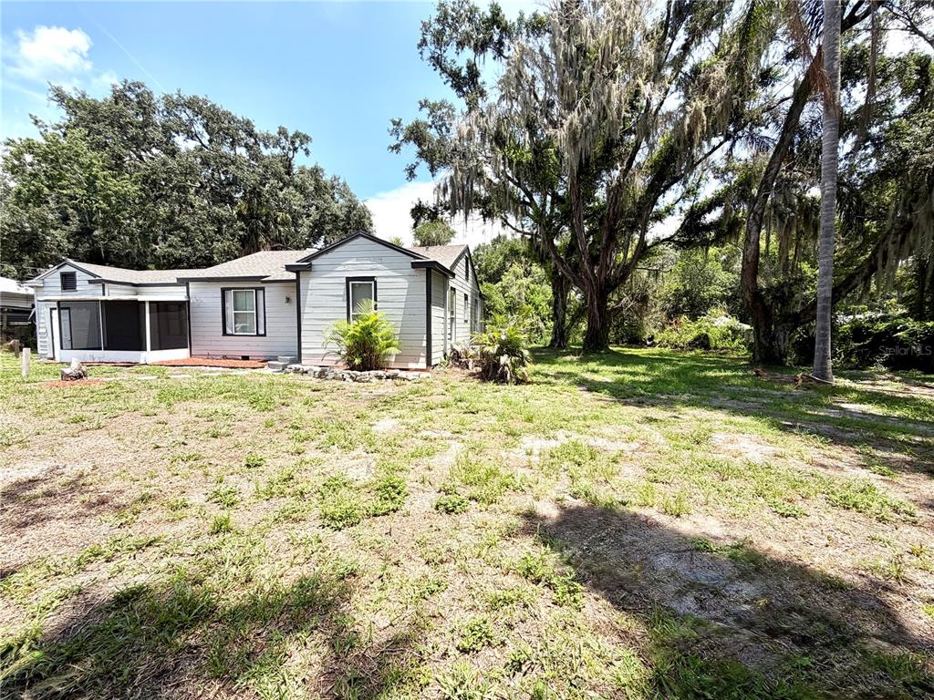 A single-story white house with a screened porch sits on a large, grassy lot — 629 AVENUE A NE, WINTER HAVEN, FL