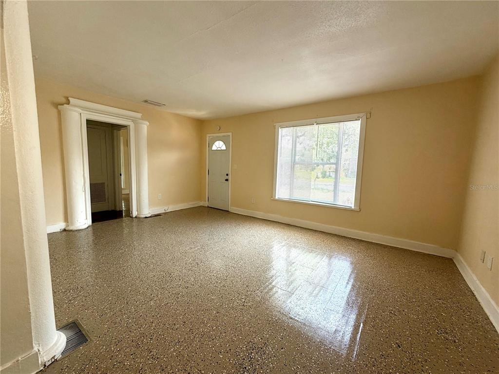 An empty room features beige walls, a speckled epoxy floor, and a white doorway — 629 AVENUE A NE, WINTER HAVEN, FL