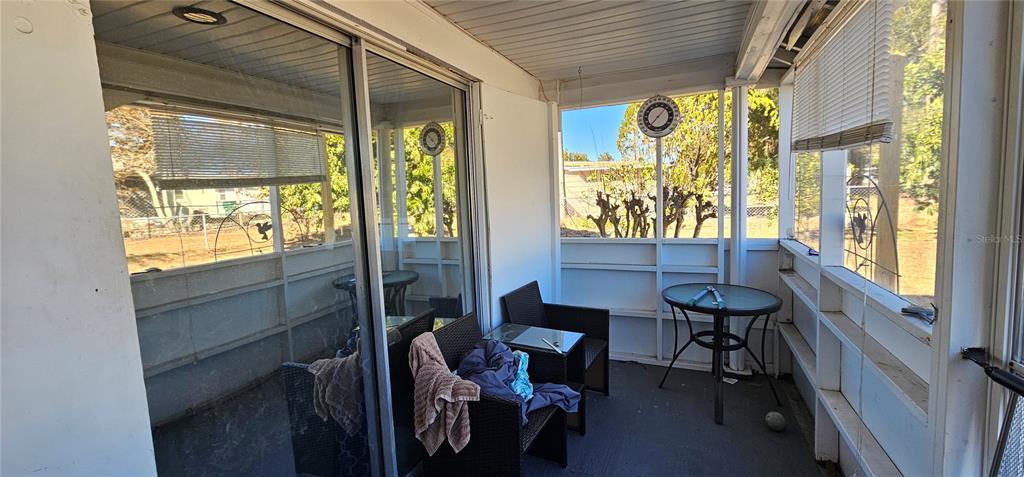 A screened-in porch features a sliding glass door, wicker furniture, and a small round table — 6020 17TH STREET, ZEPHYRHILLS, FL
