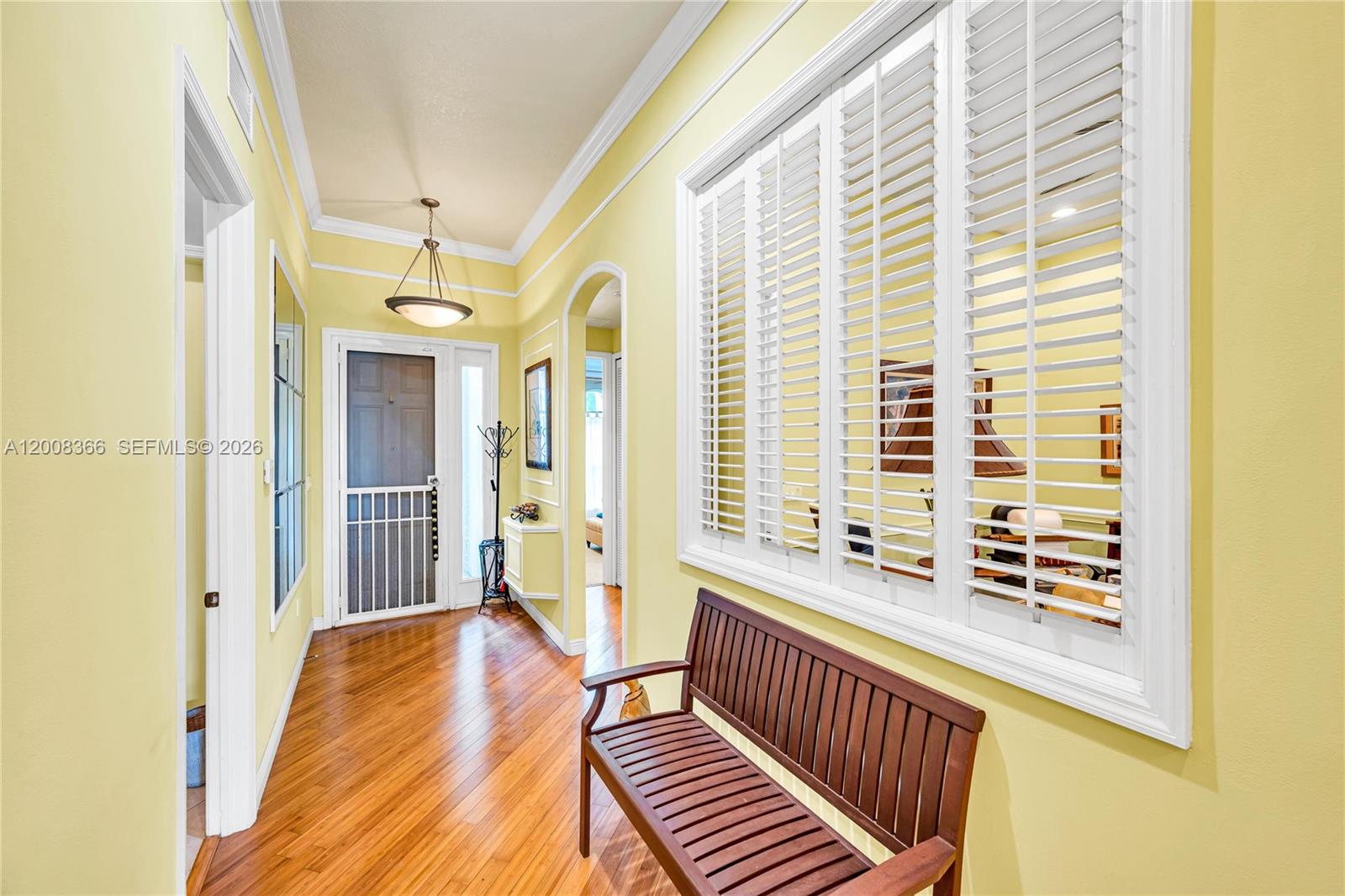 A hallway with yellow walls, hardwood floors, a wooden bench, and white plantation shutters — 3465 NE 2nd St, Homestead FL 33033, HOMESTEAD, FL