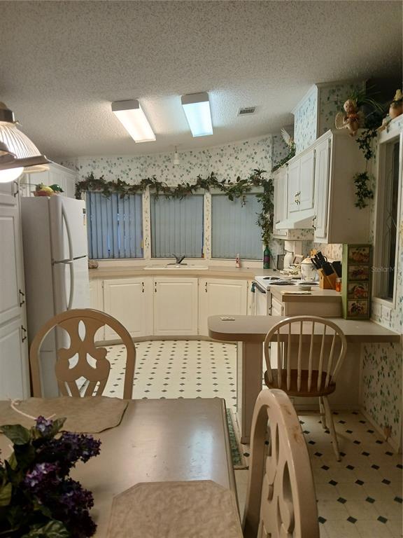 A kitchen features white cabinets, a corner sink, patterned wallpaper, and a small breakfast bar — 5415 JACOB AVENUE, POLK CITY, FL