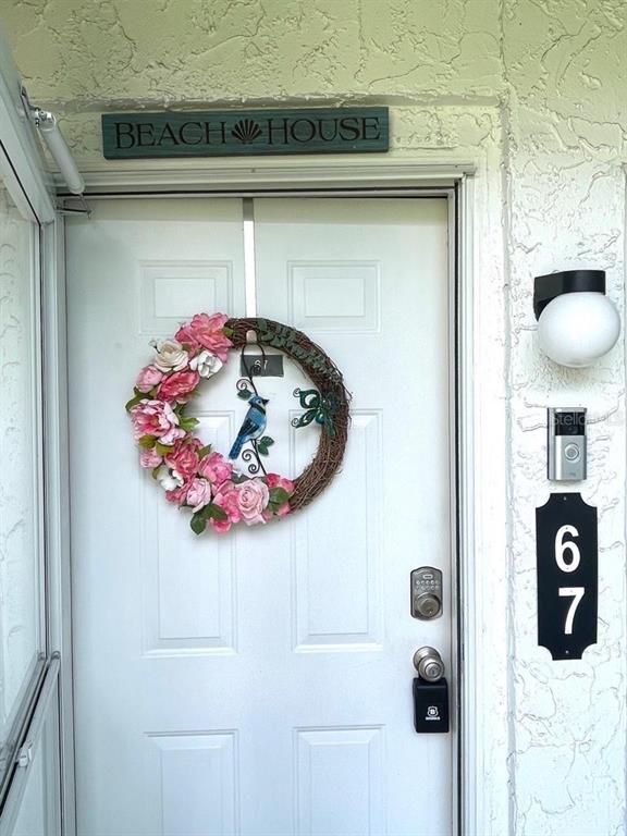 A white front door features a floral wreath, a beach house sign, and a doorbell camera — 840 CENTER AVENUE UNIT 67, HOLLY HILL, FL