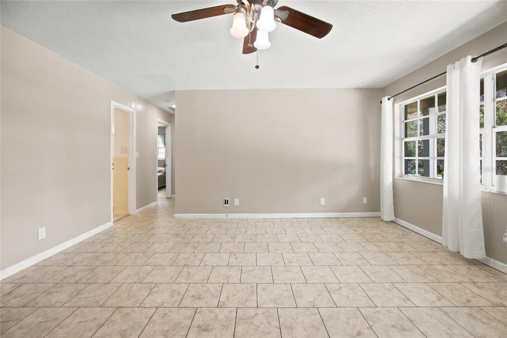 An empty room with beige walls, tile flooring, a ceiling fan, and large windows — 723 SE 30TH AVENUE, OCALA, FL