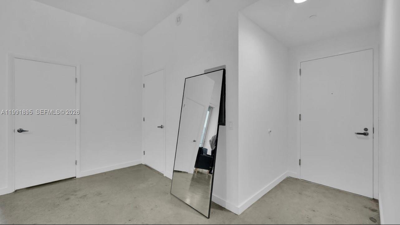 A minimalist room with white walls, concrete floors, three closed doors, and a floor mirror — 151 SE 1st St # 2411, Miami FL 33131, MIAMI, FL
